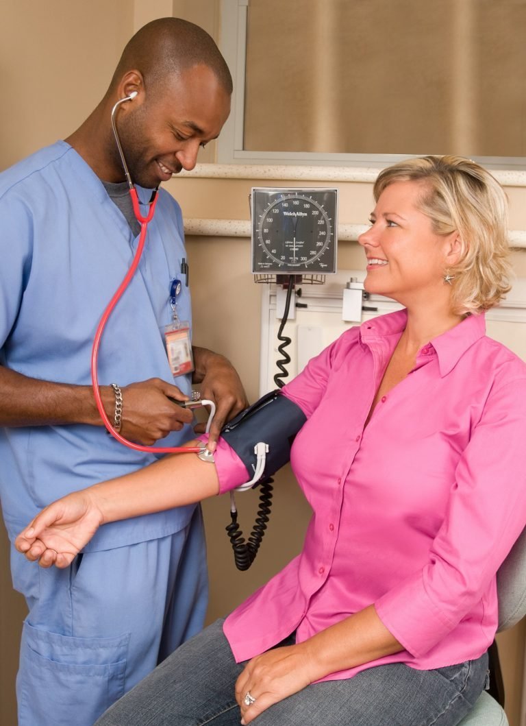 A healthcare worker checking a smiling patient’s blood pressure in a clinic
